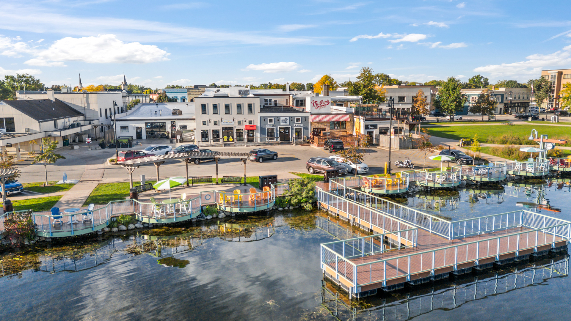 Colorful circular seating pods with yellow, orange and blue chairs above the water on the Oconomowoc lakefront, with the Six Little Ducks storefront visible in the background