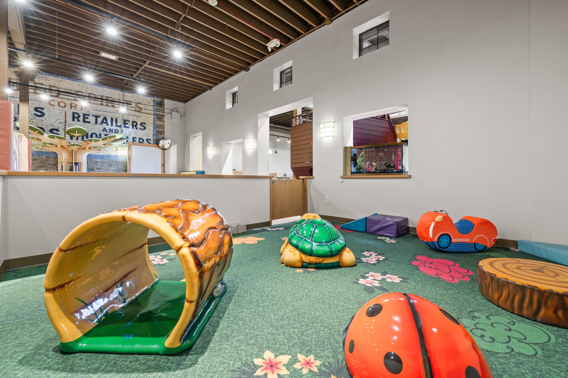 Tots area with a log tunnel, turtle rider and soft toys for toddlers at Six Little Ducks in Oconomowoc